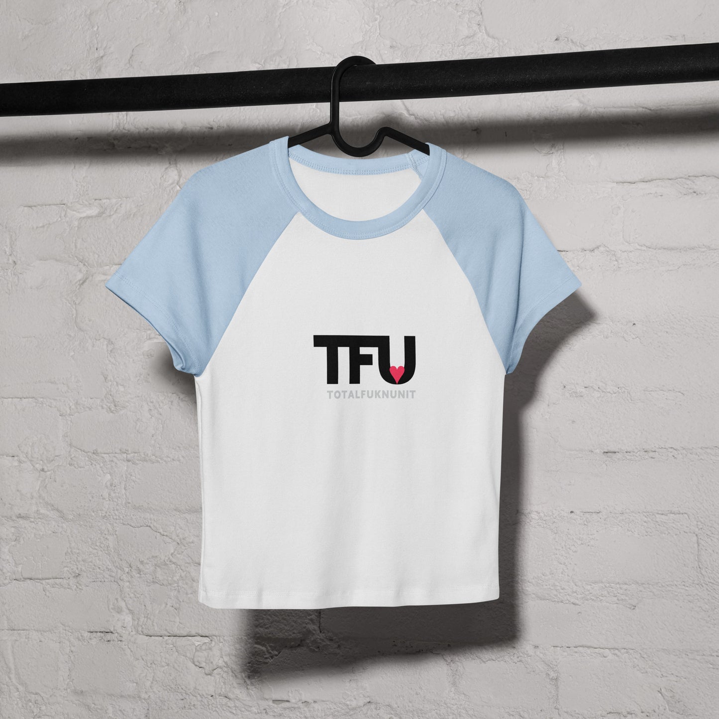 White and light blue baseball shirt with 'TFU' logo on a hanger against a gray concrete wall.